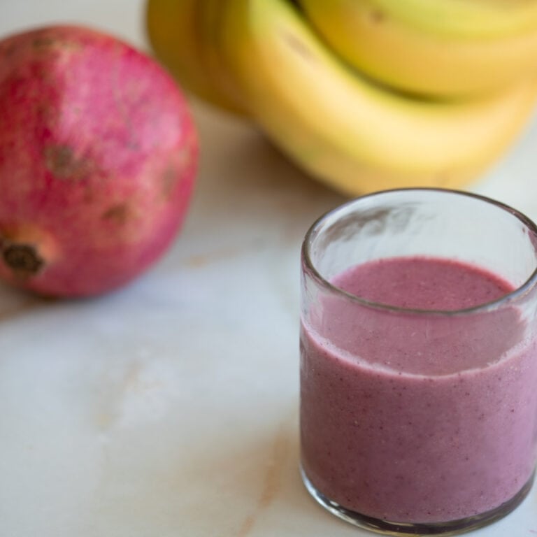 strawberry pomegranate smoothie with a banana and pomegranate in the background