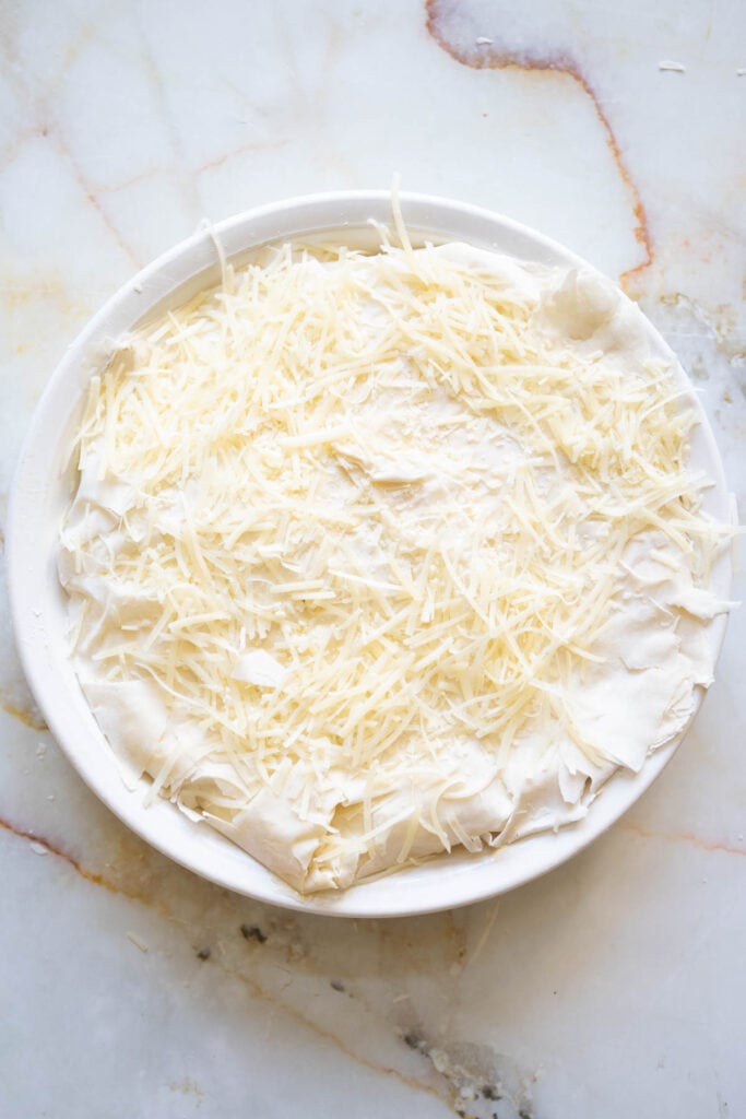 adding some parmesan cheese on top of the Greek spinach and feta pie