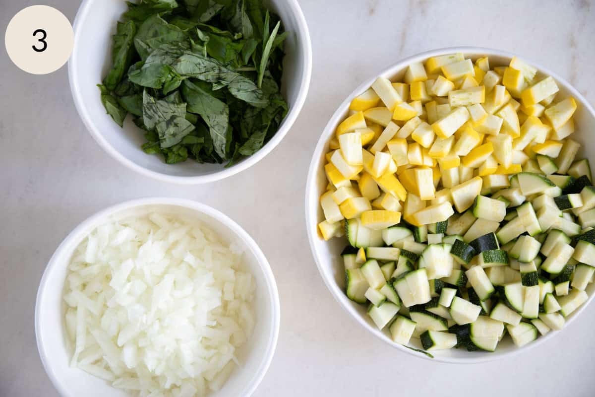 chopped zucchini, chopped squash, chopped onions, and chopped basil in bowls
