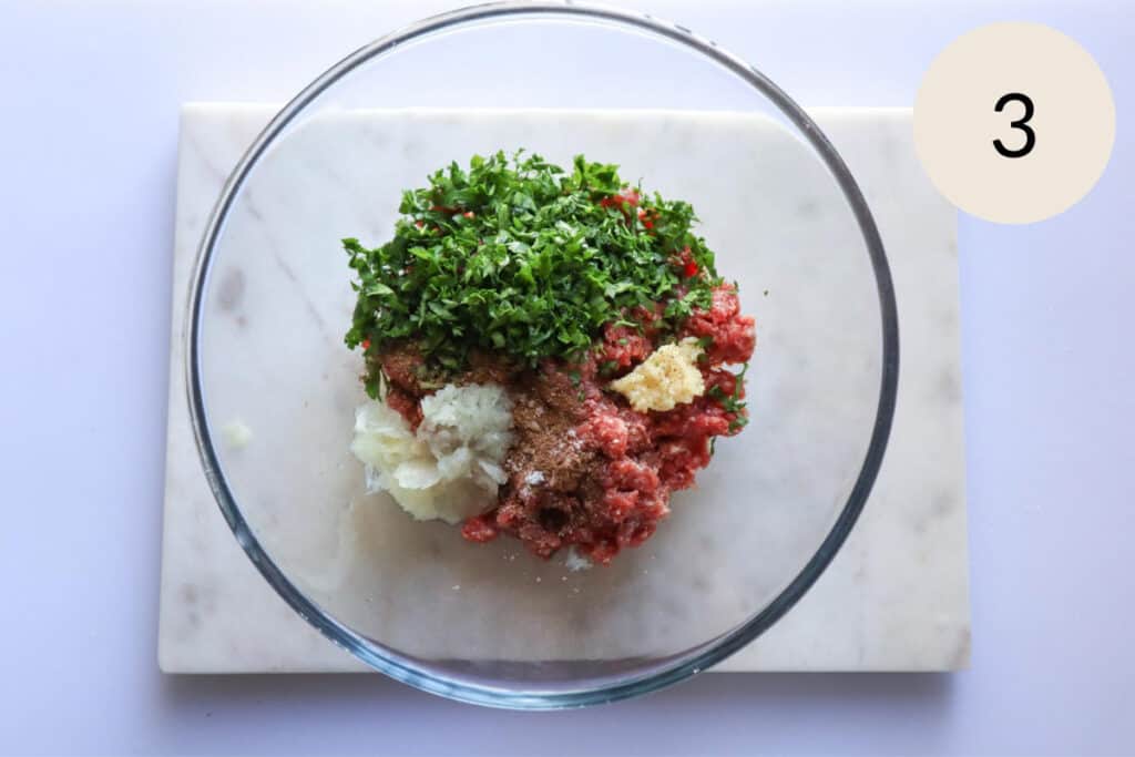 add the spices, mashed garlic, and onion to the ground meat