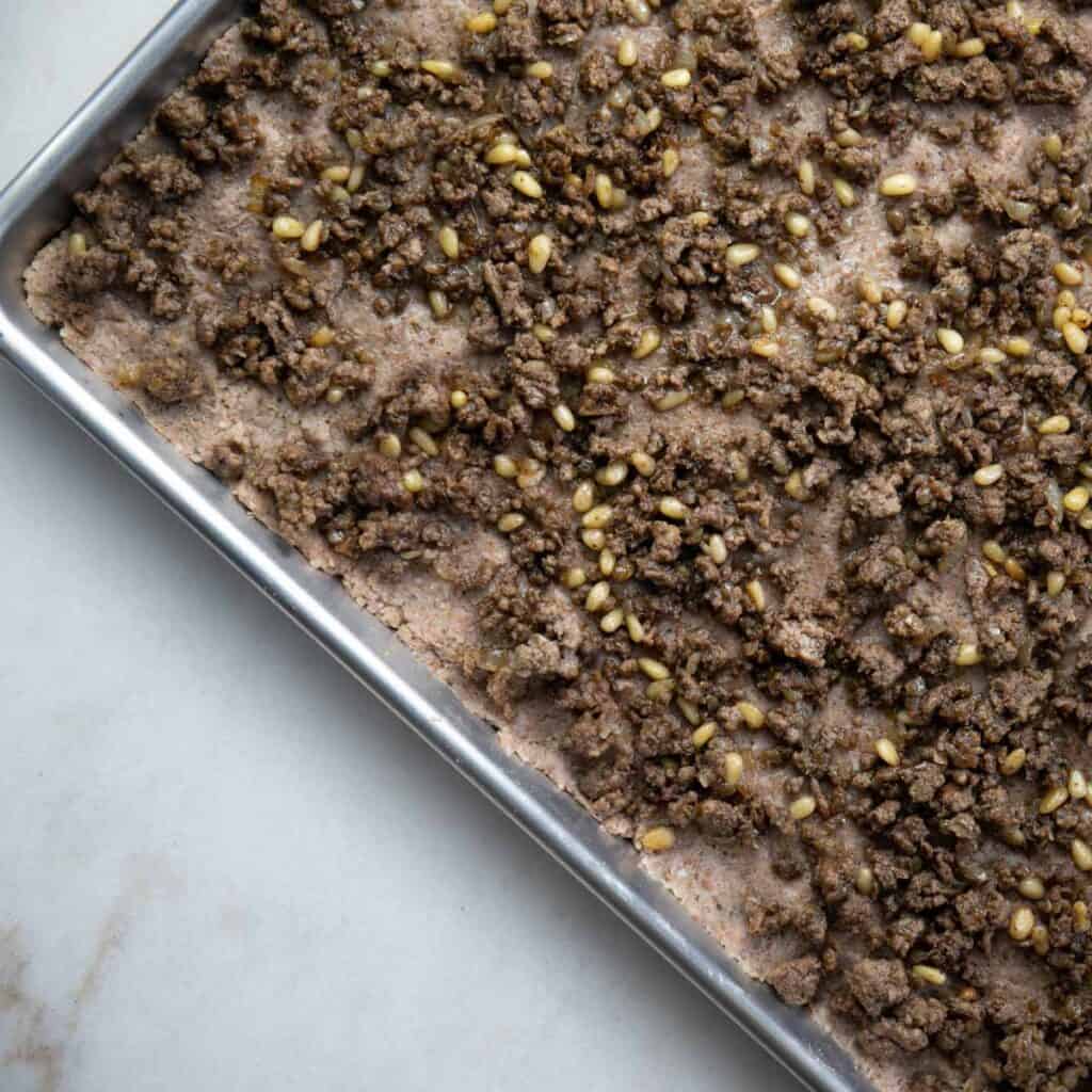layer the minced meat, pine nuts, and onion on the base kibbeh mixture
