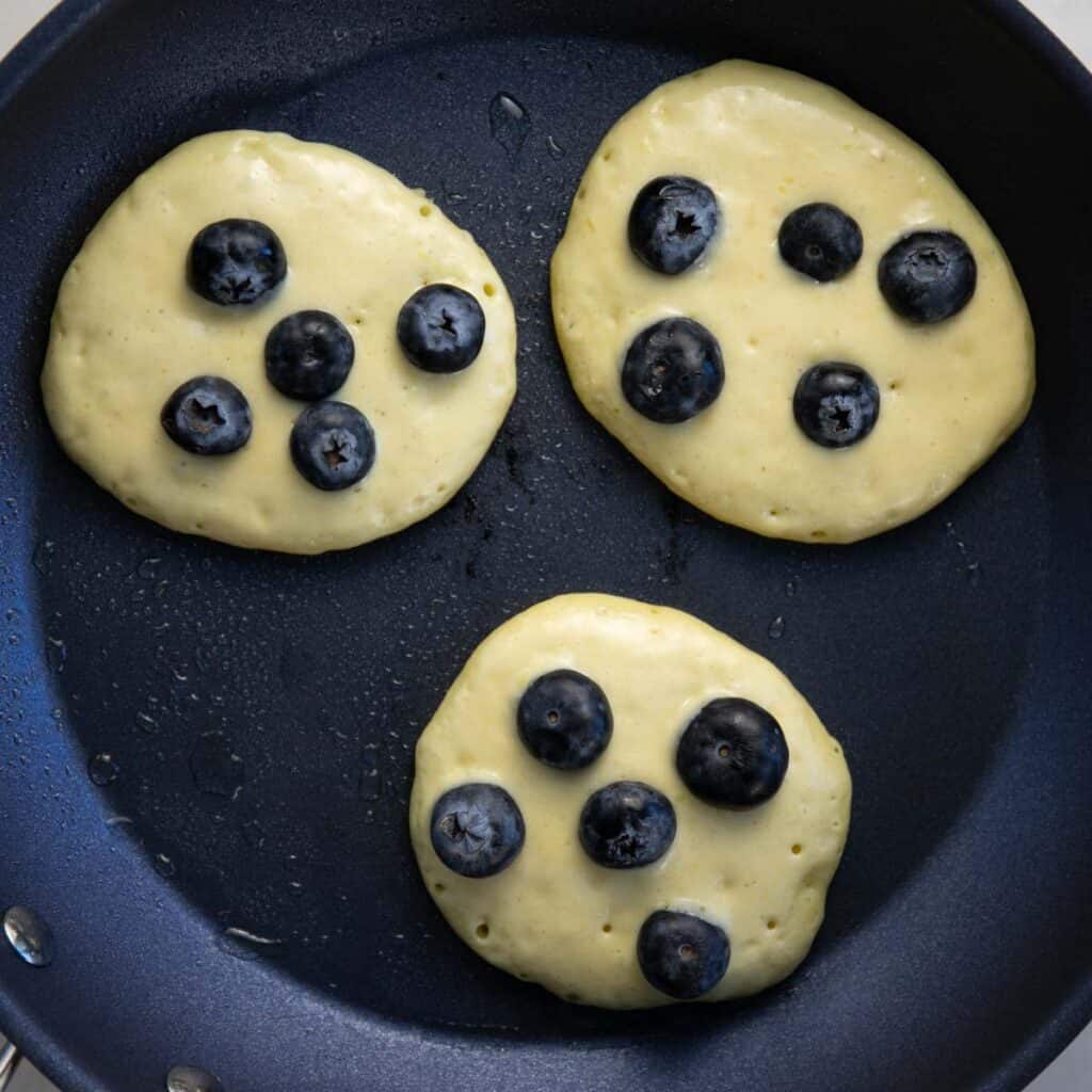 making 3 blueberry pancakes in a greased pan