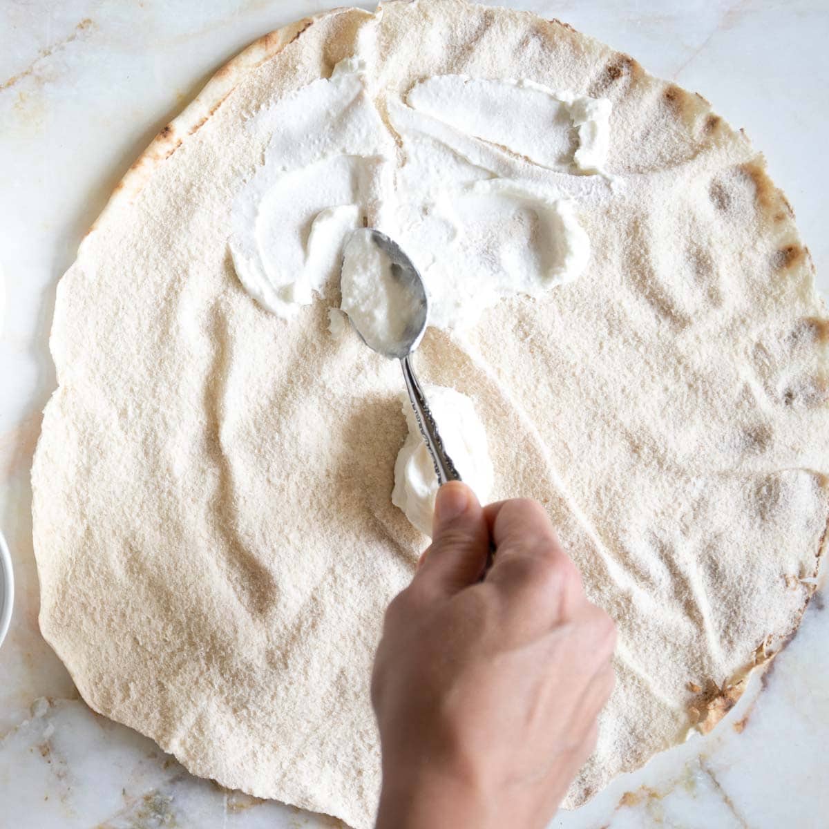 spreading labneh dip on lebanese pita bread.