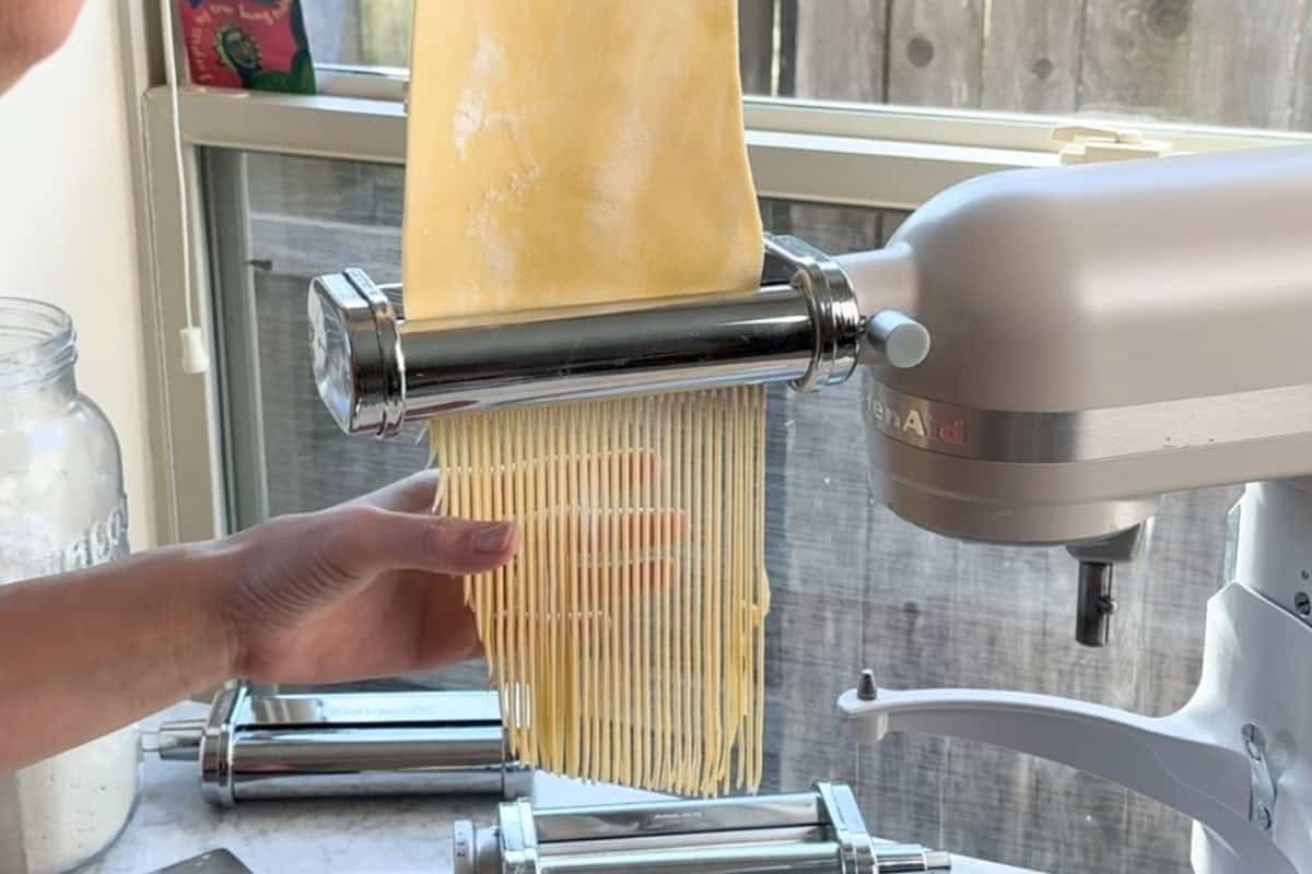 using the spaghetti attachment to cut the pasta sheet into spaghetti noodles.