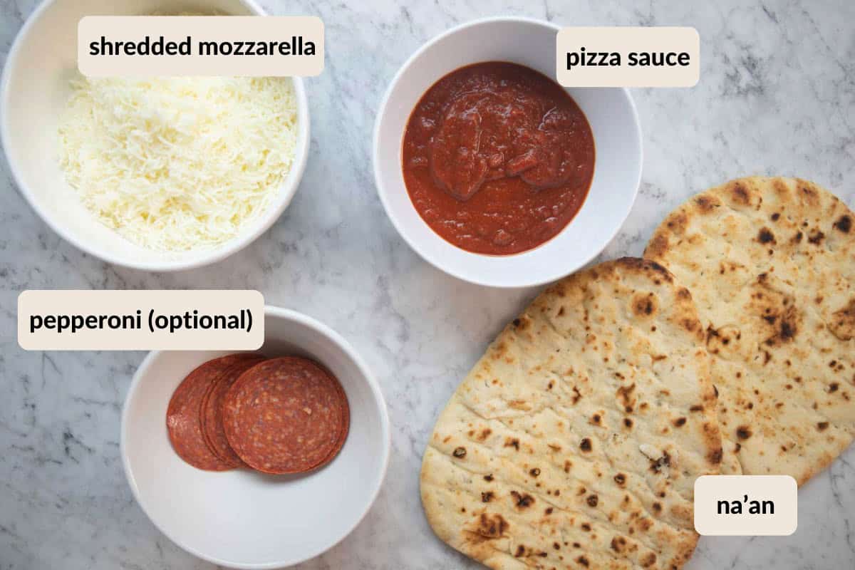 na'an flatbread, pizza sauce, shredded mozzarella, and sliced pepperoni on the counter.