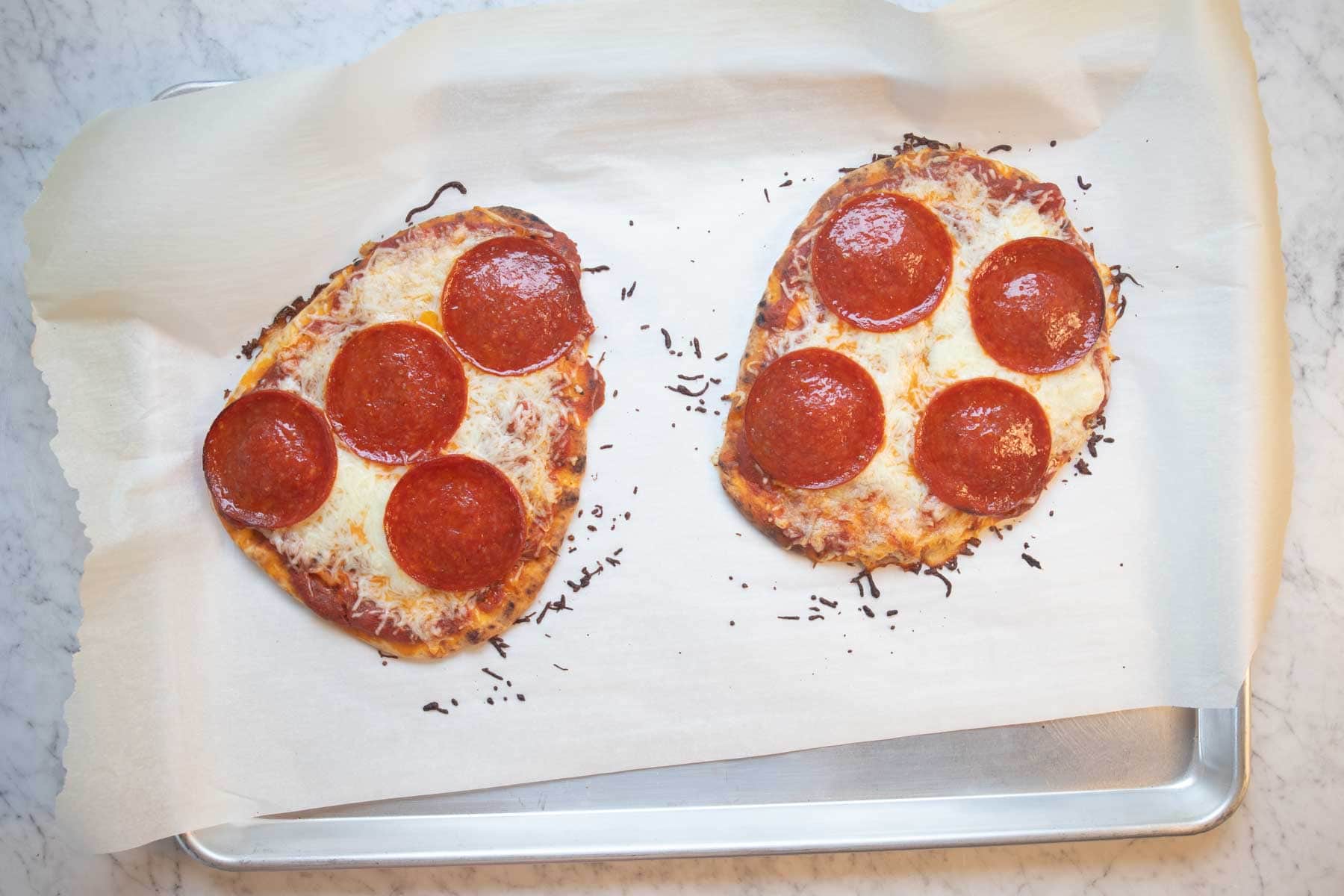 two naan bread pizzas on a baking sheet.