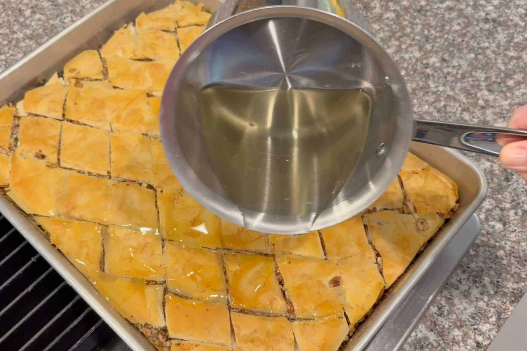 pouring the simple syrup in the cracks of the baked cinnamon pecan baklava.