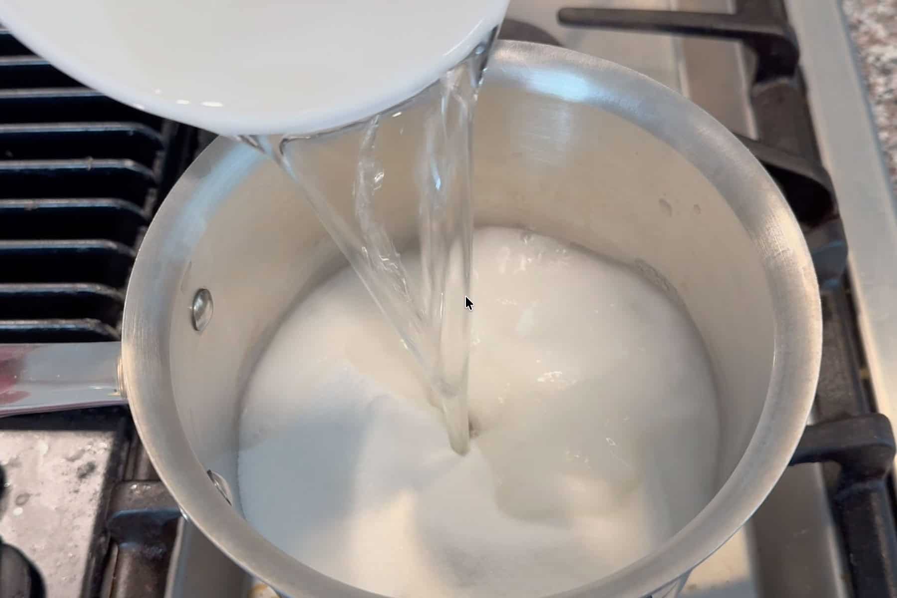 Adding water to sugar in a pot.