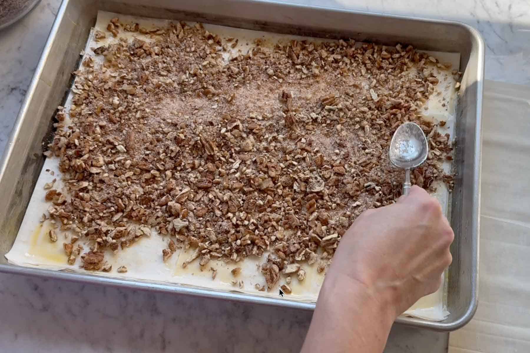 spreading the crushed pecans, cinnamon, and sugar mixture on top of the phyllo sheets.