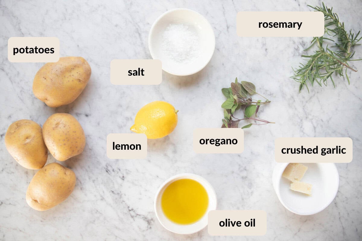 ingredients for lemon spatchcock chicken including whole potatoes, fresh rosemary, fresh oregano, lemon, olive oil, crushed garlic, and salt.
