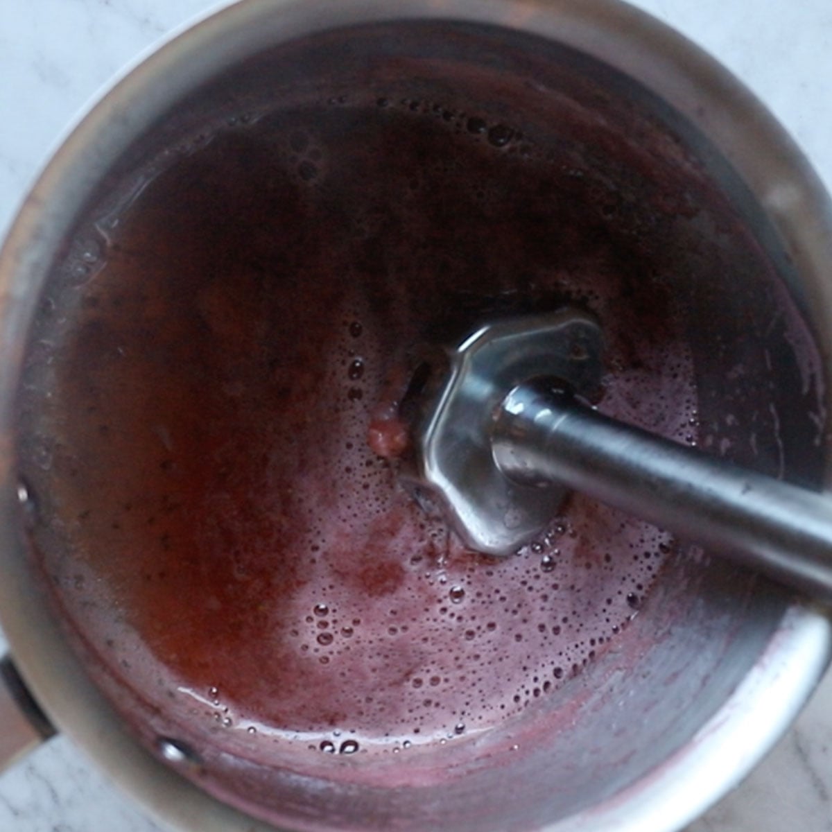 blending the strawberry sauce using a handheld immersion blender.